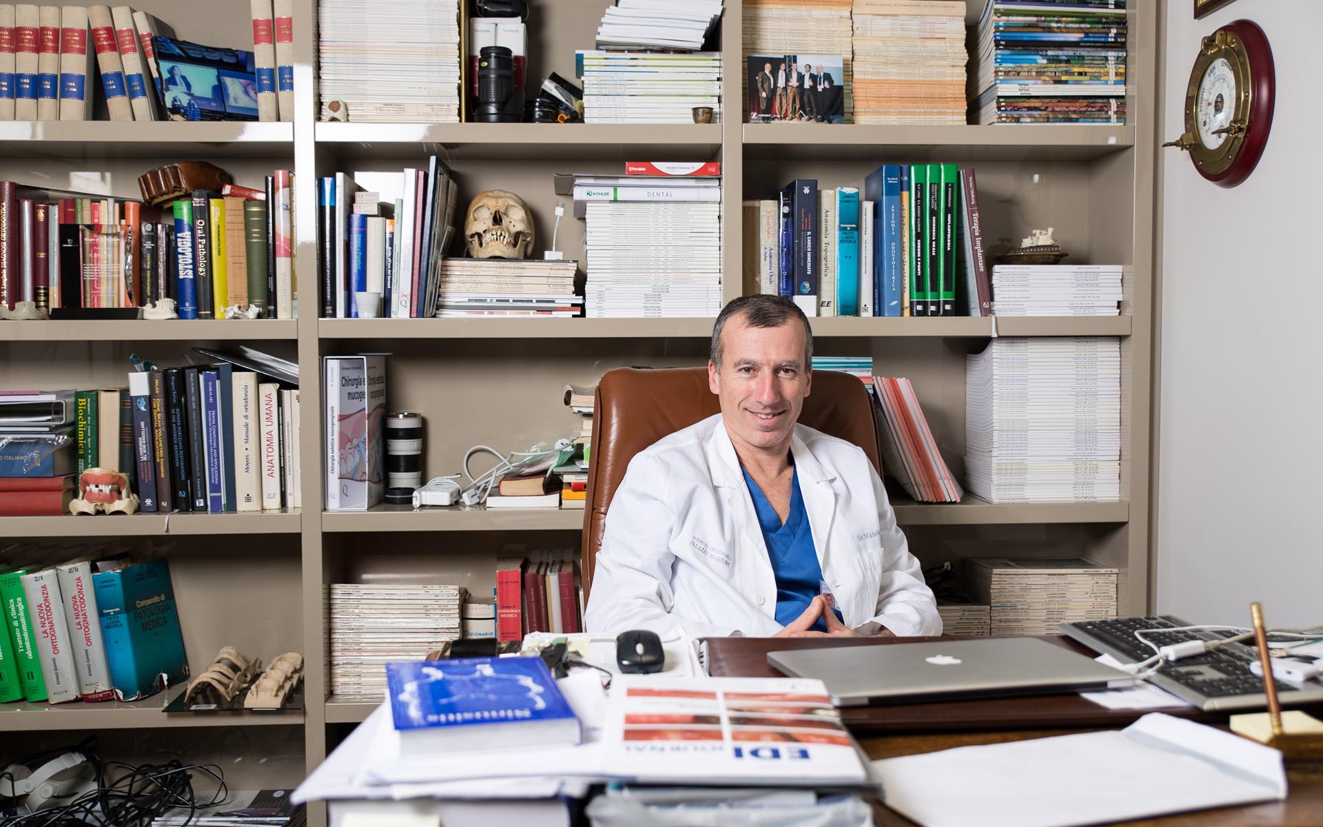 Lekarz dentstra Dr Michele Jacotti siedzący w swoim biurze, w tle biblioteczka z książkami