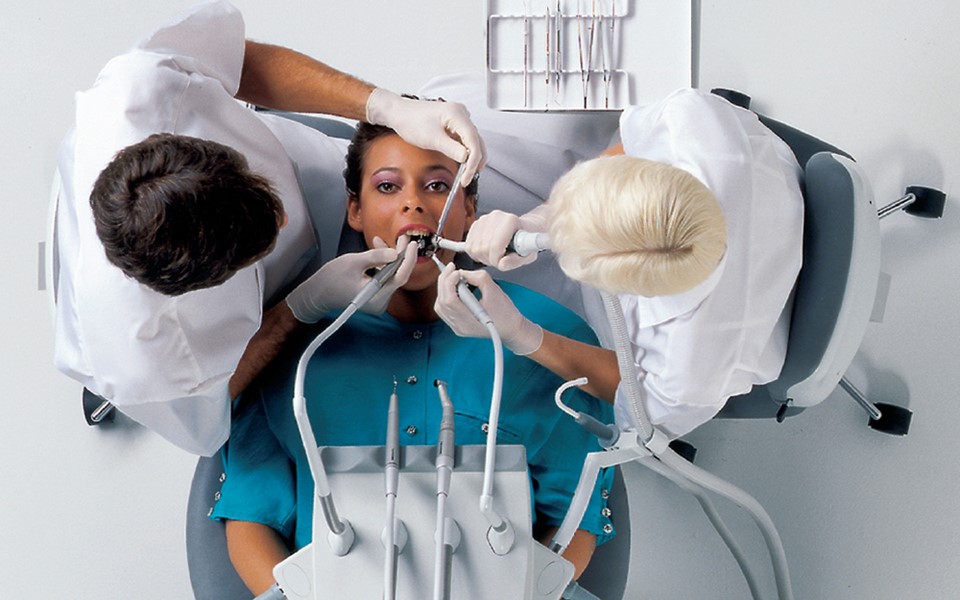 Zespół stomatologiczny pracujący na cztery ręce z pacjentką leżącą na fotelu