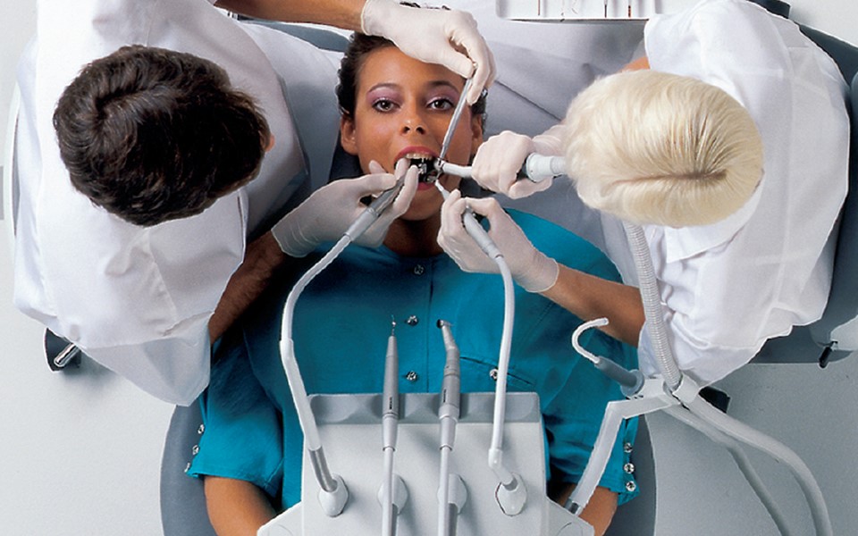 Pacjent podczas zabiegu leżący na fotelu stomatologicznym Flex Integral i dentysta z asystą wykonujący zabieg